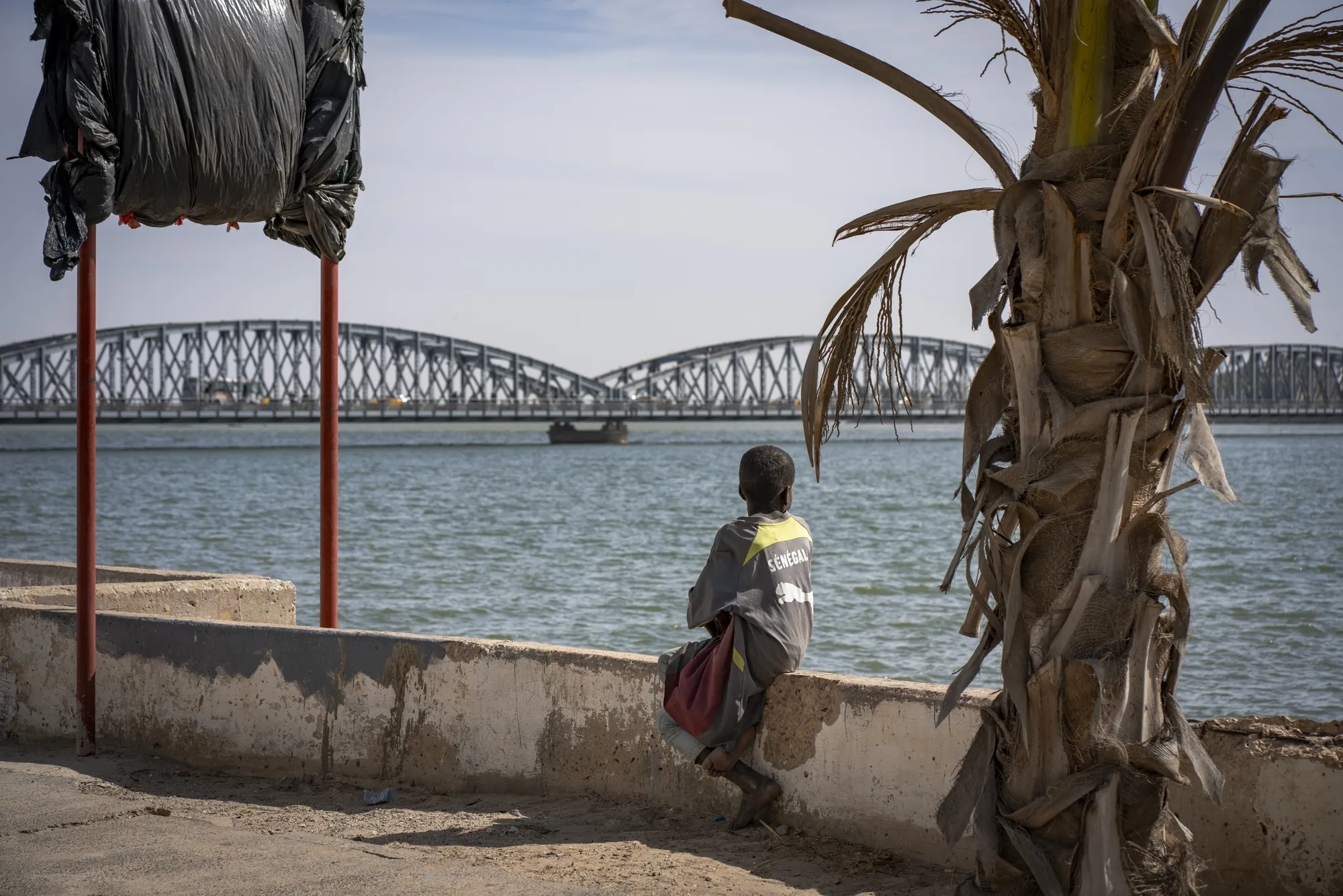 Un enfant assis face au fleuve Sénégal, devant le pont Faidherbe à Saint-Louis